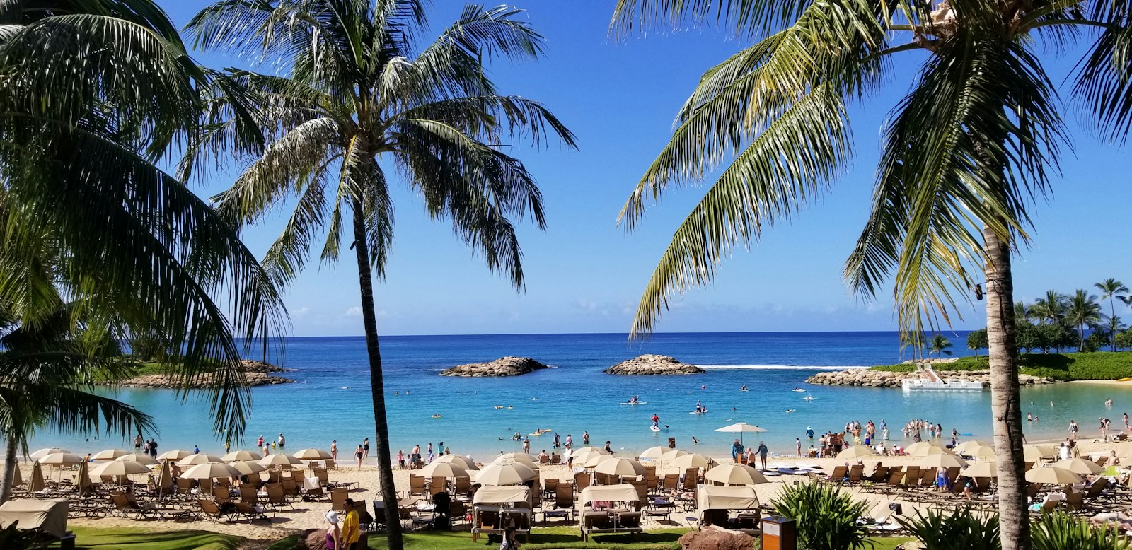 Palm trees framing the turquoise water and sandy beach at Kohola Lagoon in Ko Olina